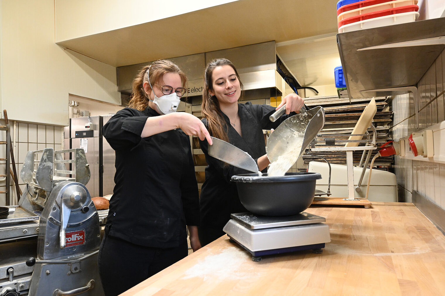 Bäckerinnen füllen gemeinsam Mehl in eine Schüssel auf einer Waage