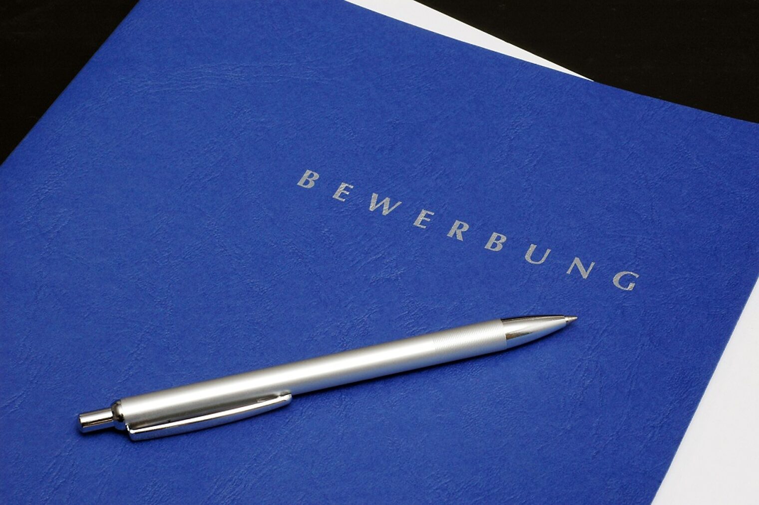 Eine königsblaue Bewerbungsmappe mit einem Kugelschreiber darauf