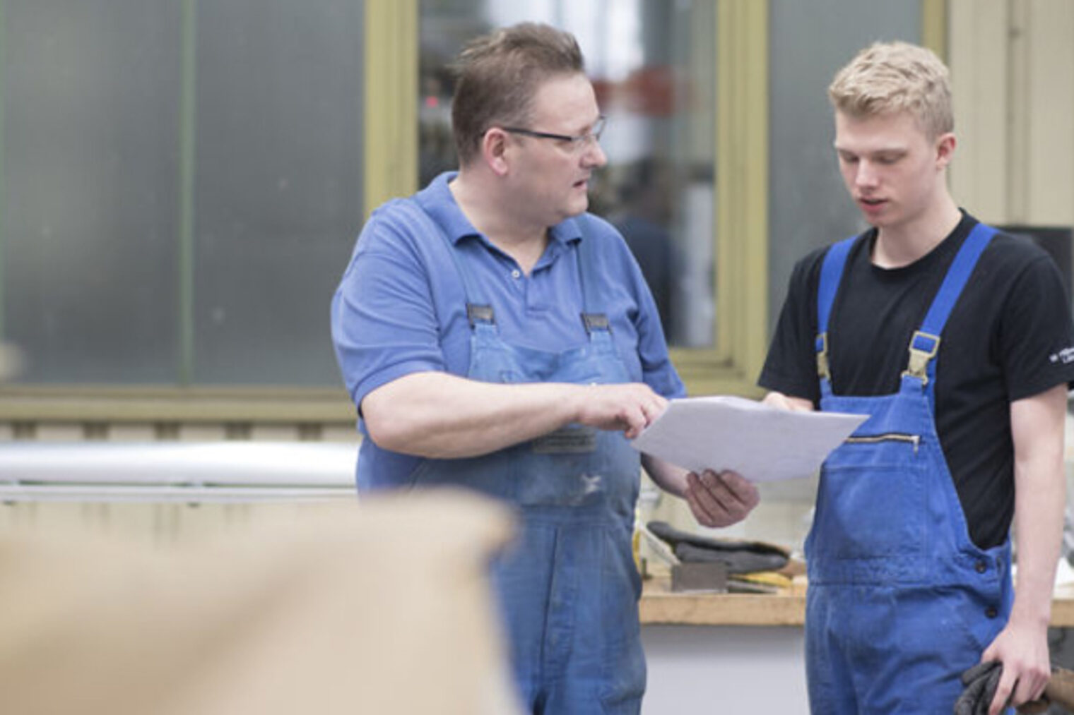 Ausbilder und Lehrling Ausbilder und Lehrling, Ausbilder zeigt dem Lehrling einen Plan, beide in Arbeitskleidung in einer Werkstatt