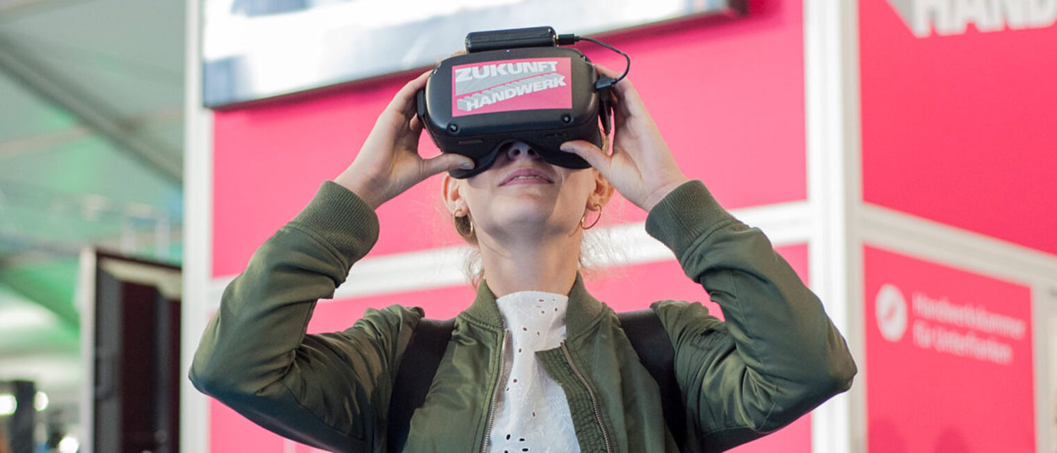 Frau mit Virtual Reality-Brille auf einer Messe vor einem Stand der Handwerkskammer für Unterfranken