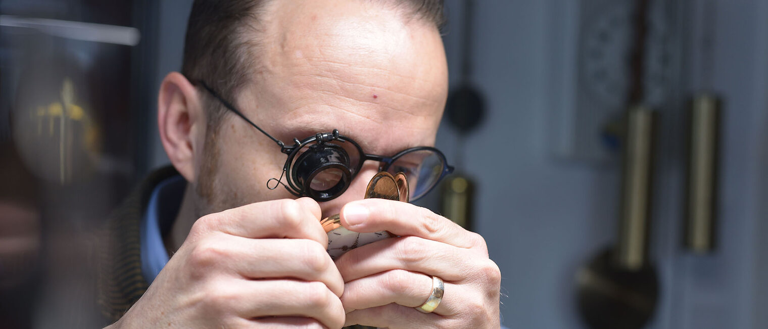 Uhrmachermeister Felix Wüstenfeld Uhrmacher in Werkstatt schaut auf Taschenuhr