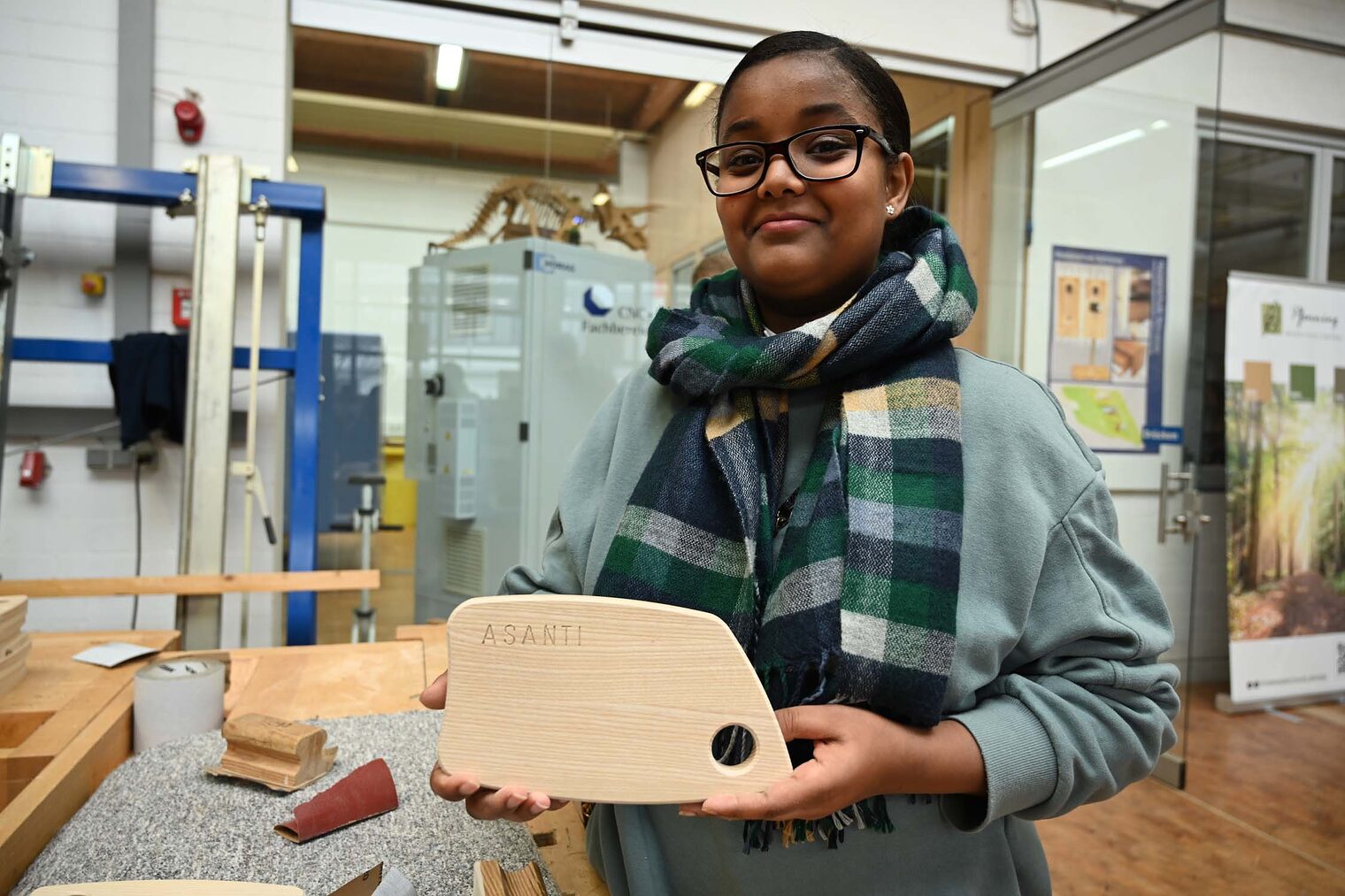 Mädchen zeigt Holzbrettchen mit eingefrästem Namen in Kamera