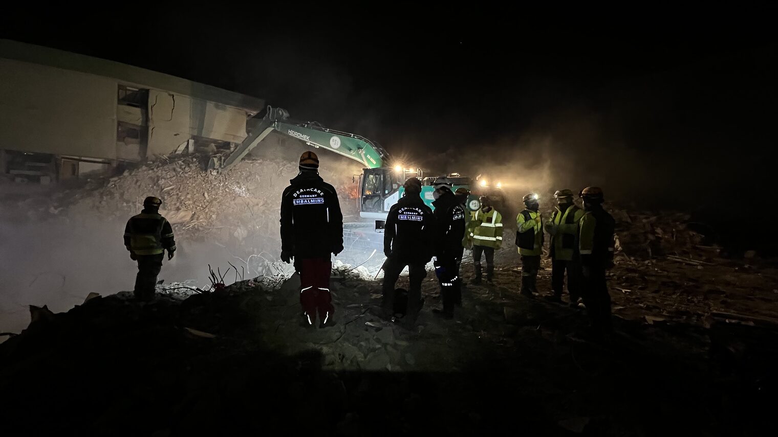 Eingestürzte Gebäude und Menschen, die bei Nacht vor einem Kran stehen.
