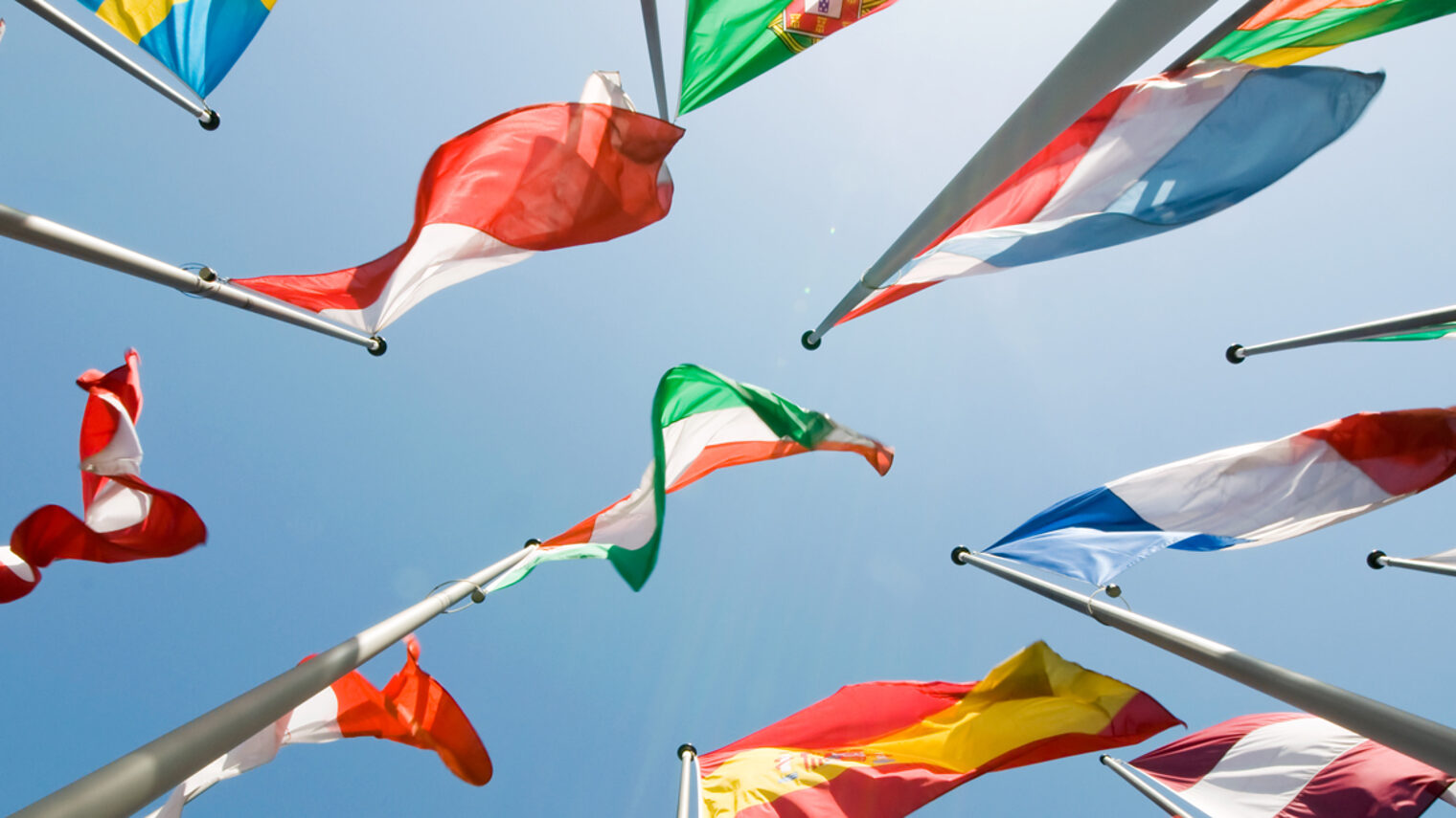 Flaggen verschiedener Länder an Fahnenmasten, fotografiert von unten