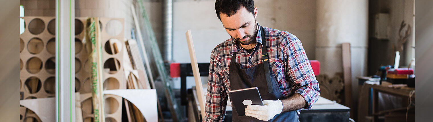 Handwerker steht in Werkstatt und schaut auf ein Tablet