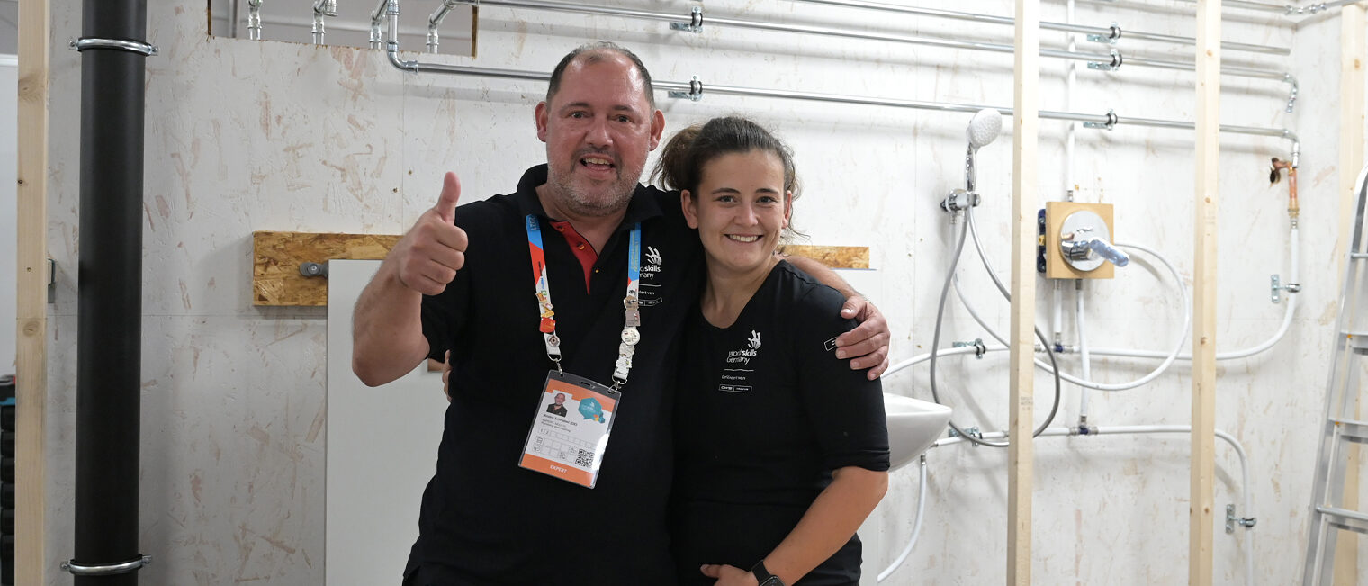 EuroSkills 2023 | Stefanie Hahn Mann und Frau stehen vor einer Installationswand und lächeln in die Kamera