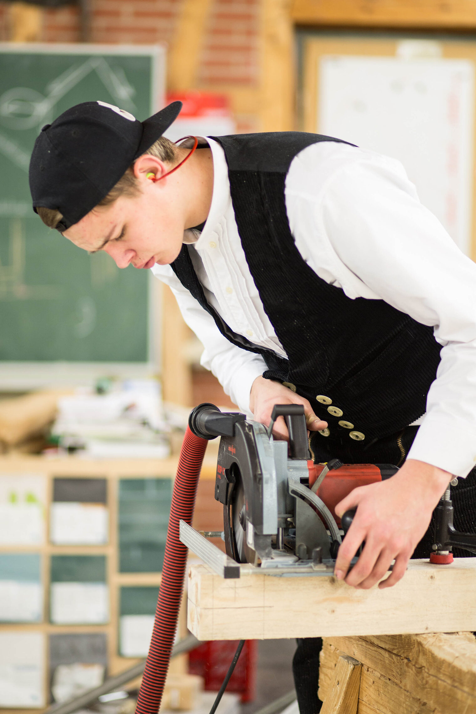 Auszubildender zum Zimmerer mit einer Säge, sägt ein Stück Holz