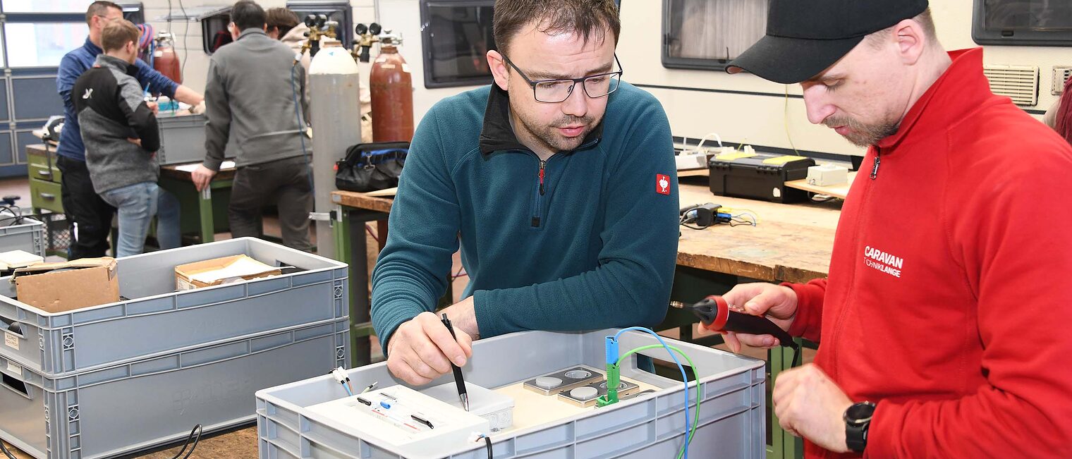 Zwei Kursteilnehmer arbeiten an einer elektrischen Schaltung, während einer von ihnen ein Messgerät benutzt