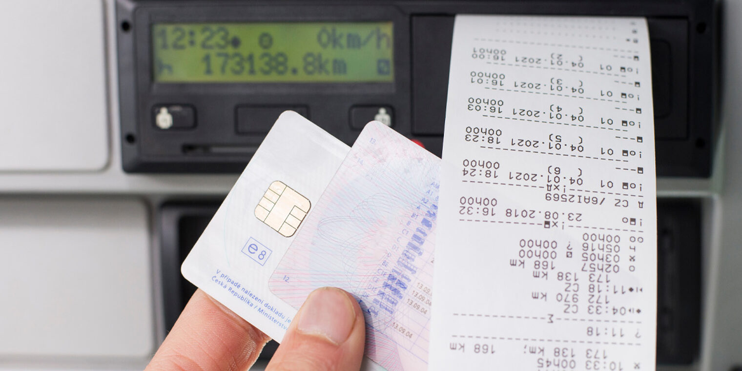 Nahaufnahme einer Hand vor einem digitalen Tachografen mit Karte und Ausdrucken