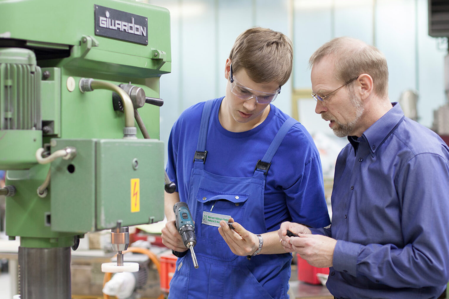 Ein Auszubildender mit Meister, in einer Werkstatt Ein Auszubildender mit seinem Meister, beide stehen in einer Werkstatt vor einer Maschine, beide tragen Schutzbrillen