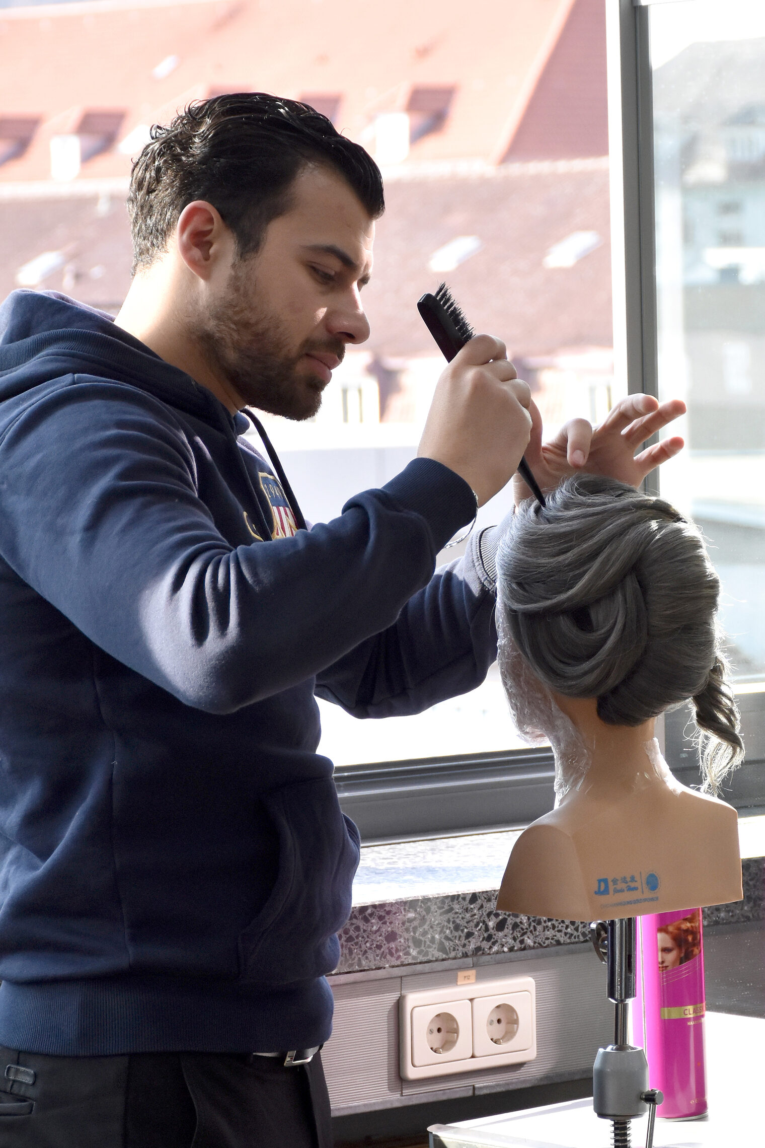 Ein angehender Friseurmeister frisiert eine Übungspuppe mit einem Kamm.