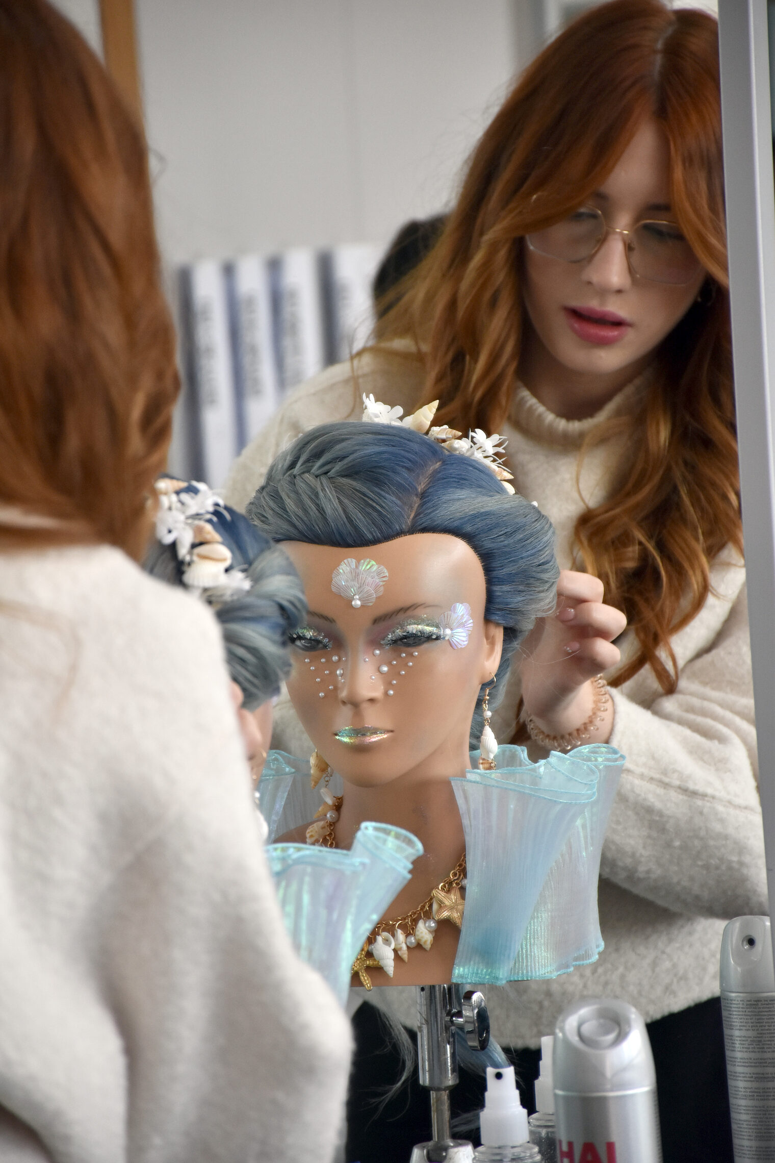 Eine angehende Friseurmeisterin stylt eine Hochsteckfrisur an einem Übungskopf mit aufwendigem Make-up und Accessoires.