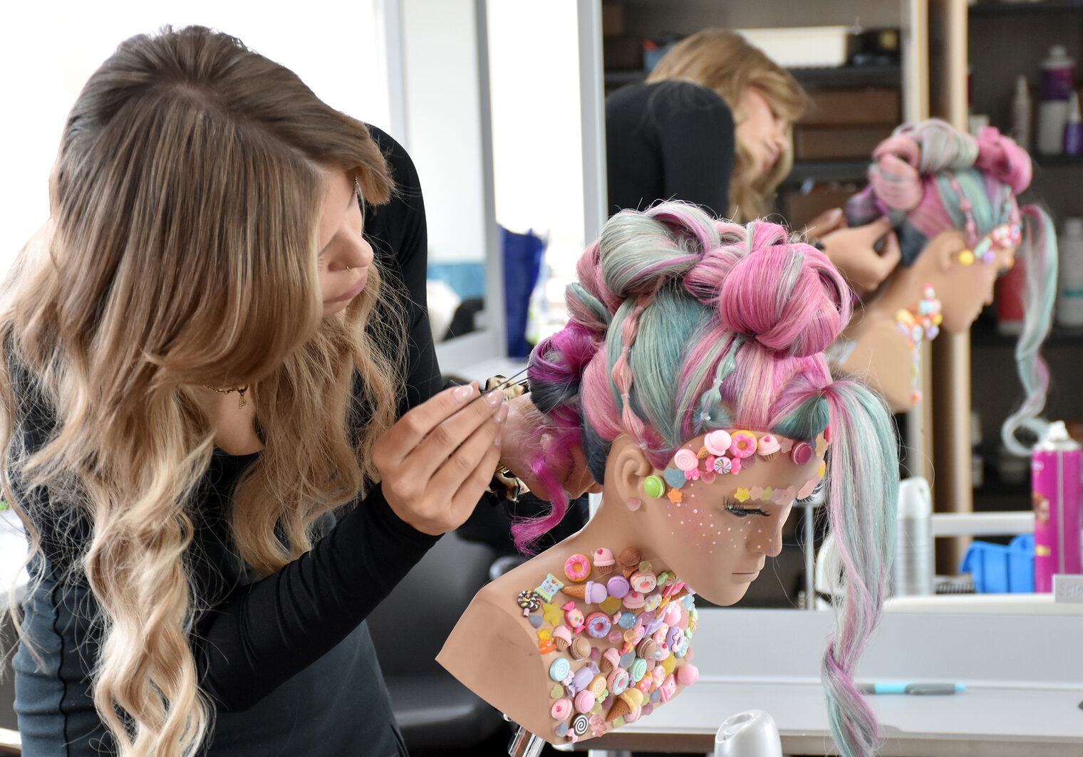 Eine angehende Friseurmeisterin frisiert konzentriert den Kopf einer Übungspuppe mit einer kunstvollen, farbenfrohen Frisur.