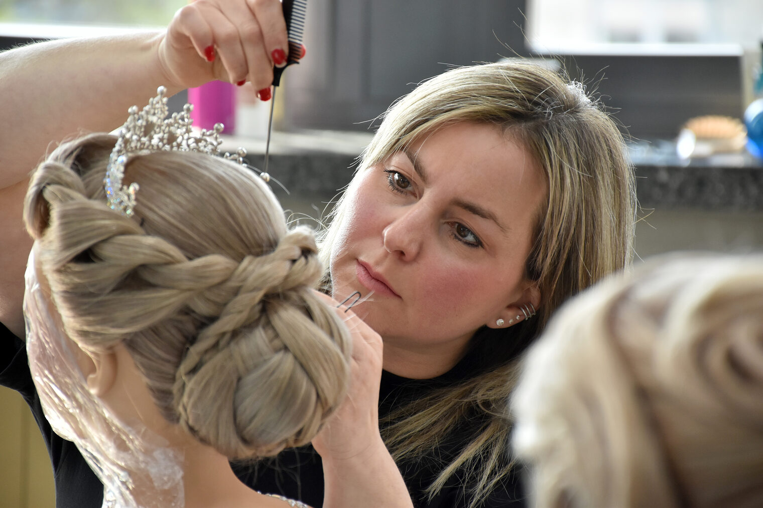 Eine angehende Friseurmeisterin rückt mit einem Kamm eine funkelnde Tiara auf dem Kopf einer Übungspuppe zurecht.