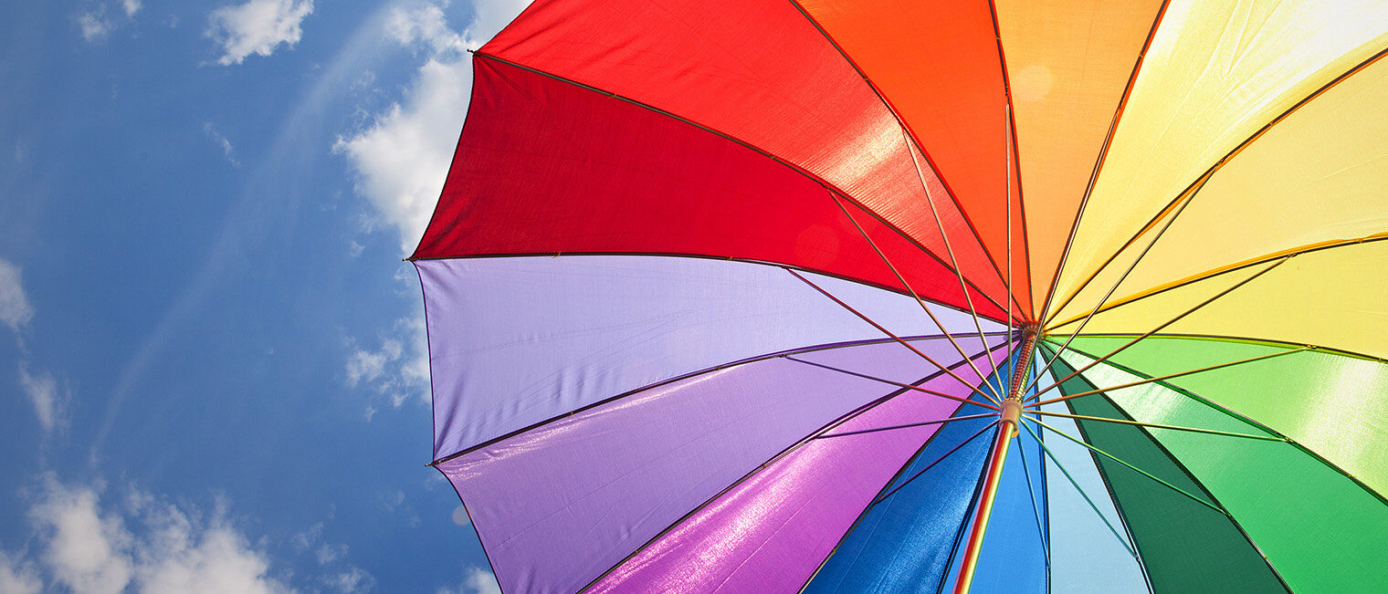 Himmel mit Sonnenschirm Bunter Sonnenschirm in Regenbogenfarben vor blauem Himmel mit Wolken