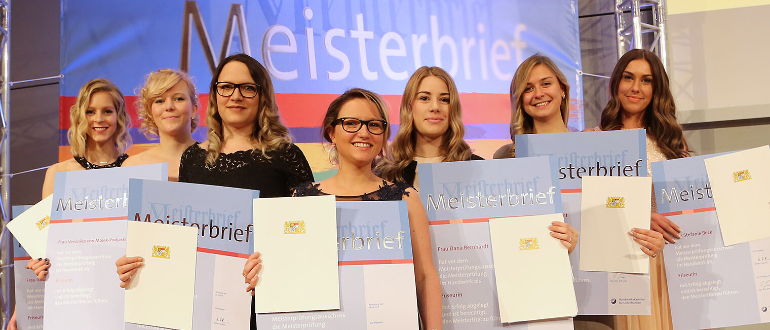 Friseur-Meisterinnen Sieben Meisterinnen im festlichen Outfit mit Meisterbriefen in der Hand, die sich über ihren Abschluss feiern.
