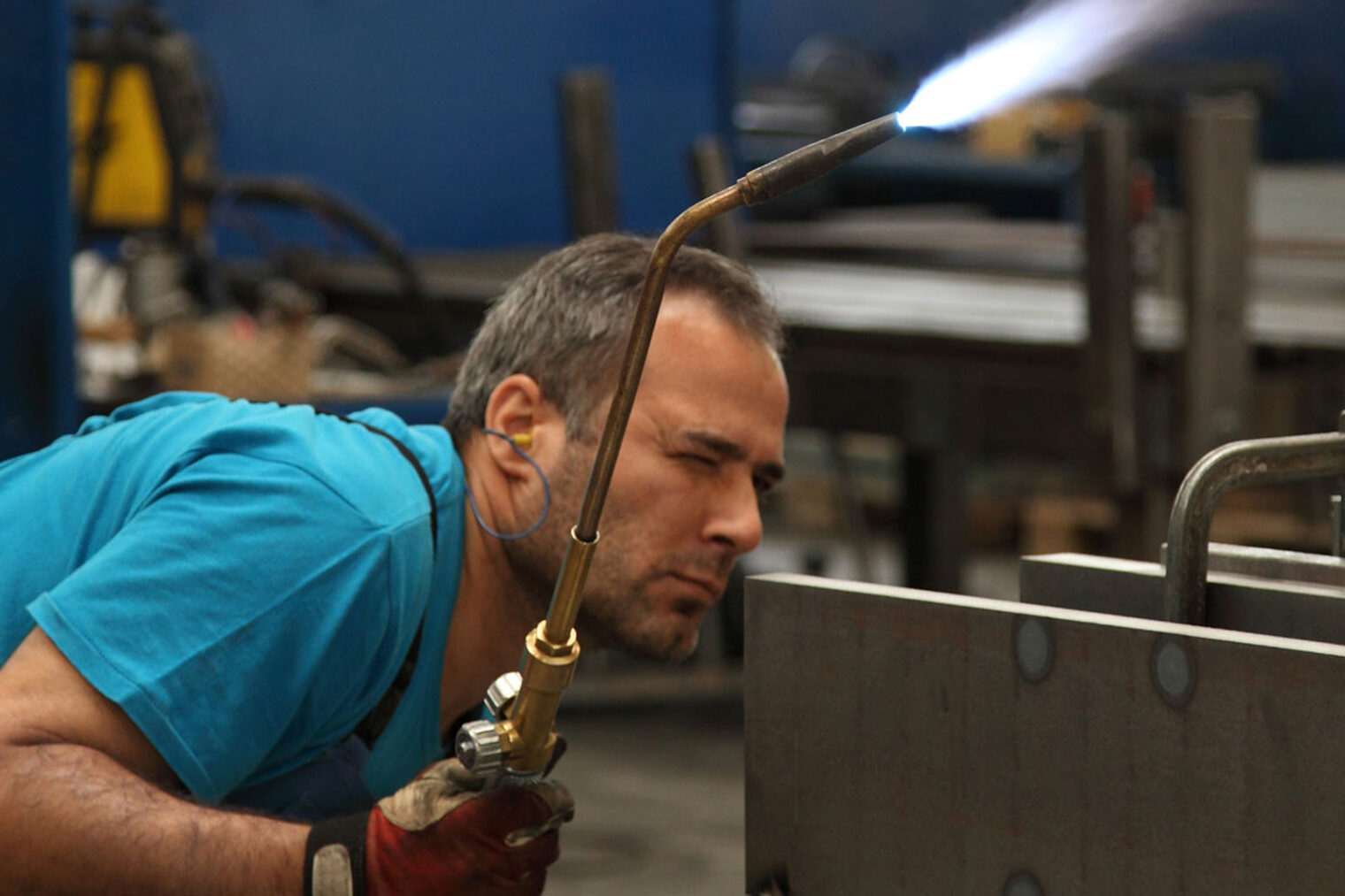 Metallbauer mit Schweißgerät in der Hand inspiziert die Schweißnaht Metallbauer in Schutzkleidung mit Schweißgerät in der rechten Hand inspiziert gebückt die Schweißnaht