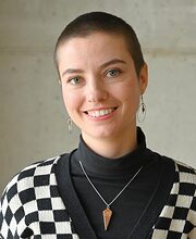 Portrait: Frau mit kurzen Haaren lächelt in die Kamera, Schwarz-Weiß karierter Pullover