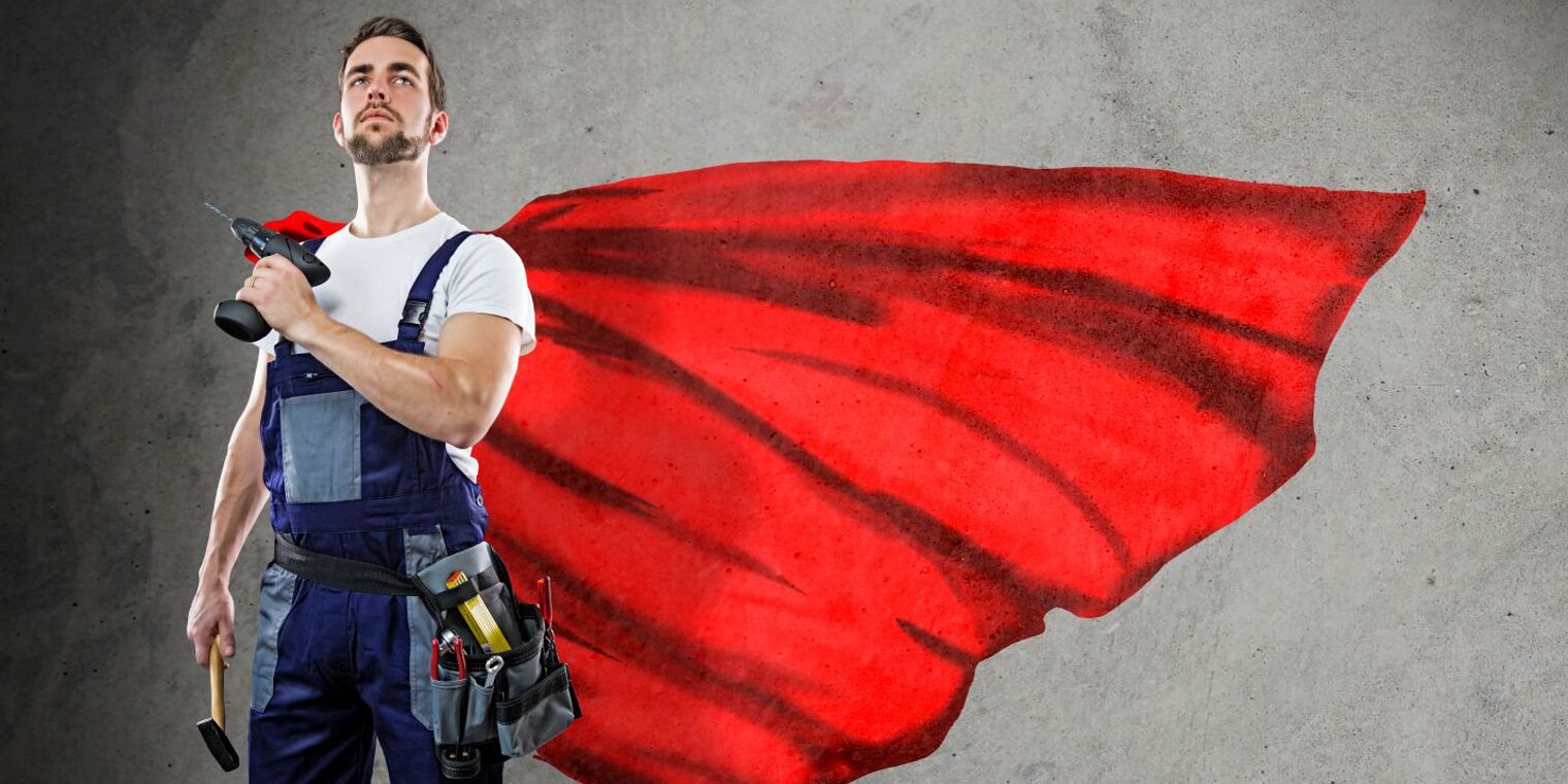 Handwerker in Blaumann mit rotem Cape und Bohrmaschine in der Hand