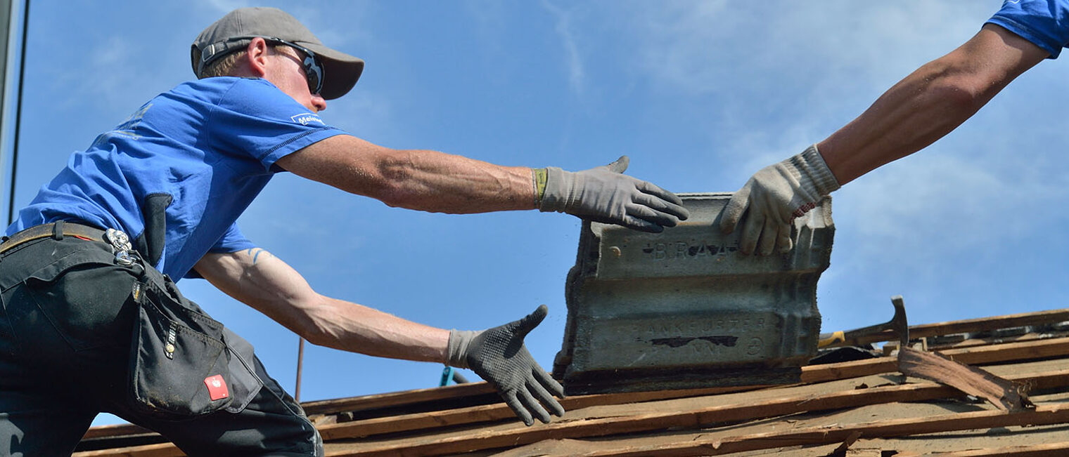 Dachdecker auf Dach reichen sich Ziegeln zu