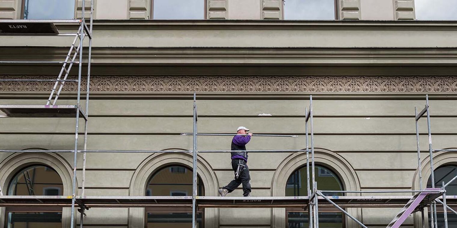 Totale von Gerüst an Gebäude mit einem darauf laufenden Gerüstbauer