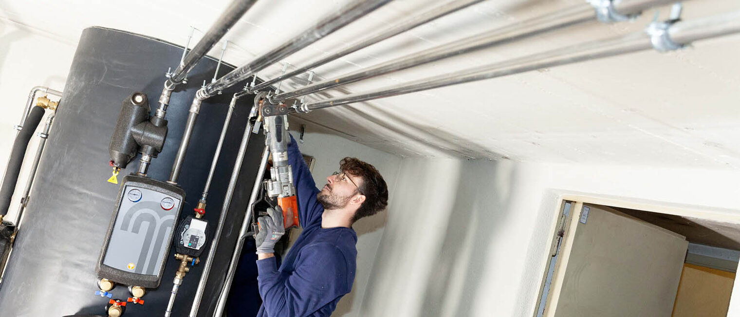 Anlagenmechaniker schraubt an Rohren eines Kessels