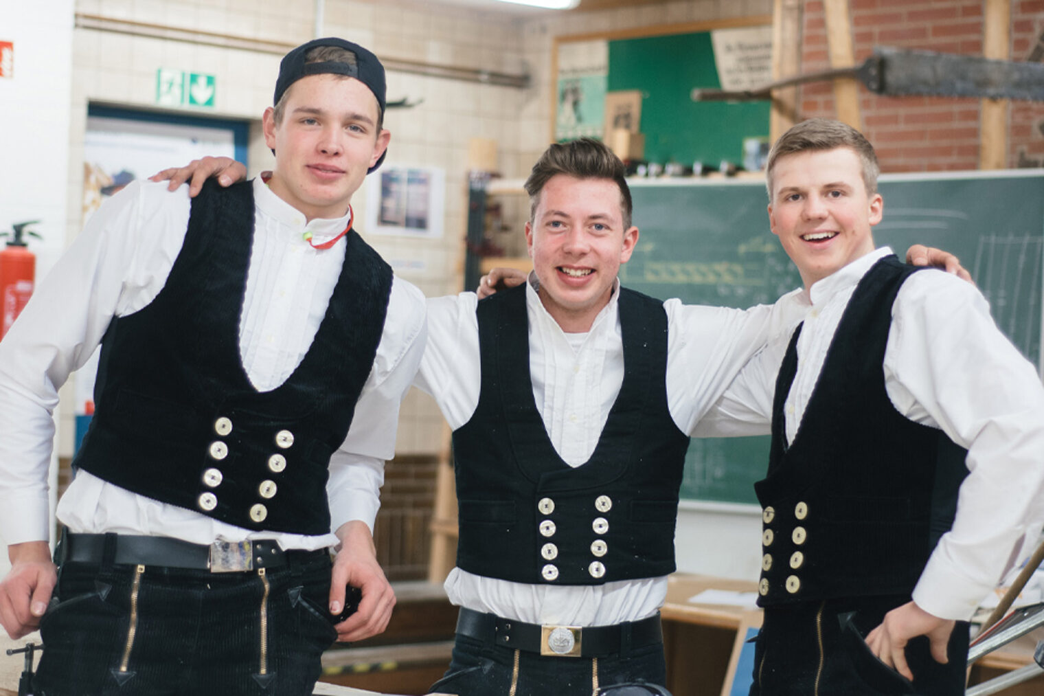 Drei Zimmerer in einer Werkstatt schauen freundschaftlich in die Kamera