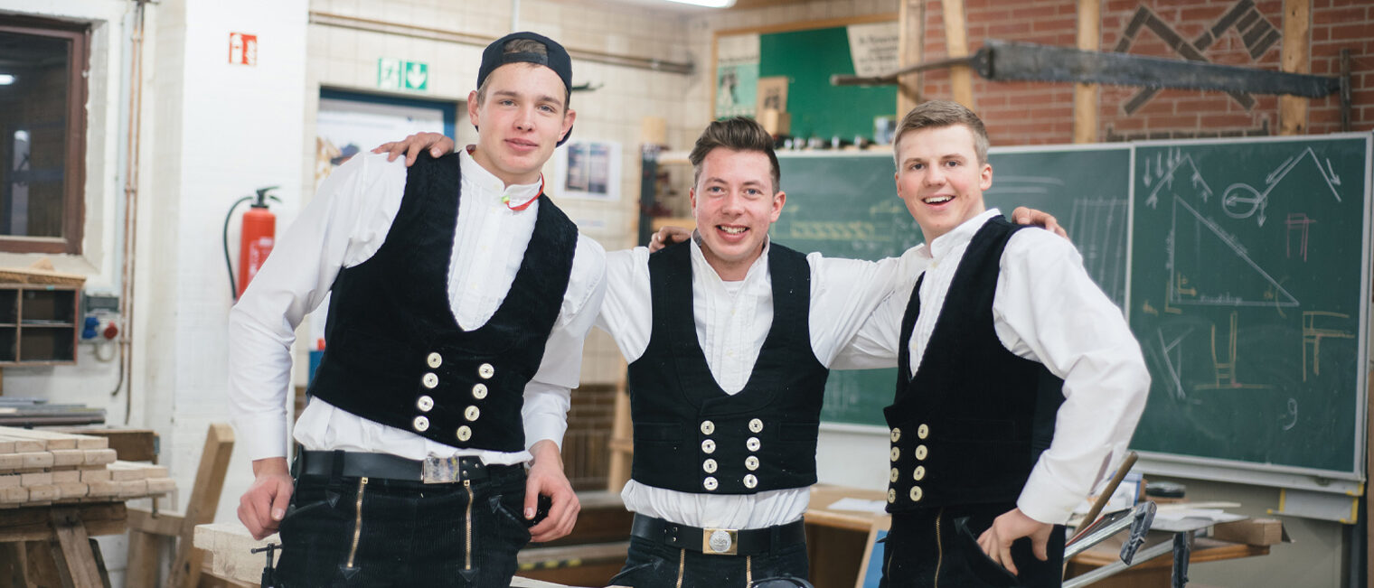 Drei Zimmerer in einer Werkstatt schauen freundschaftlich in die Kamera