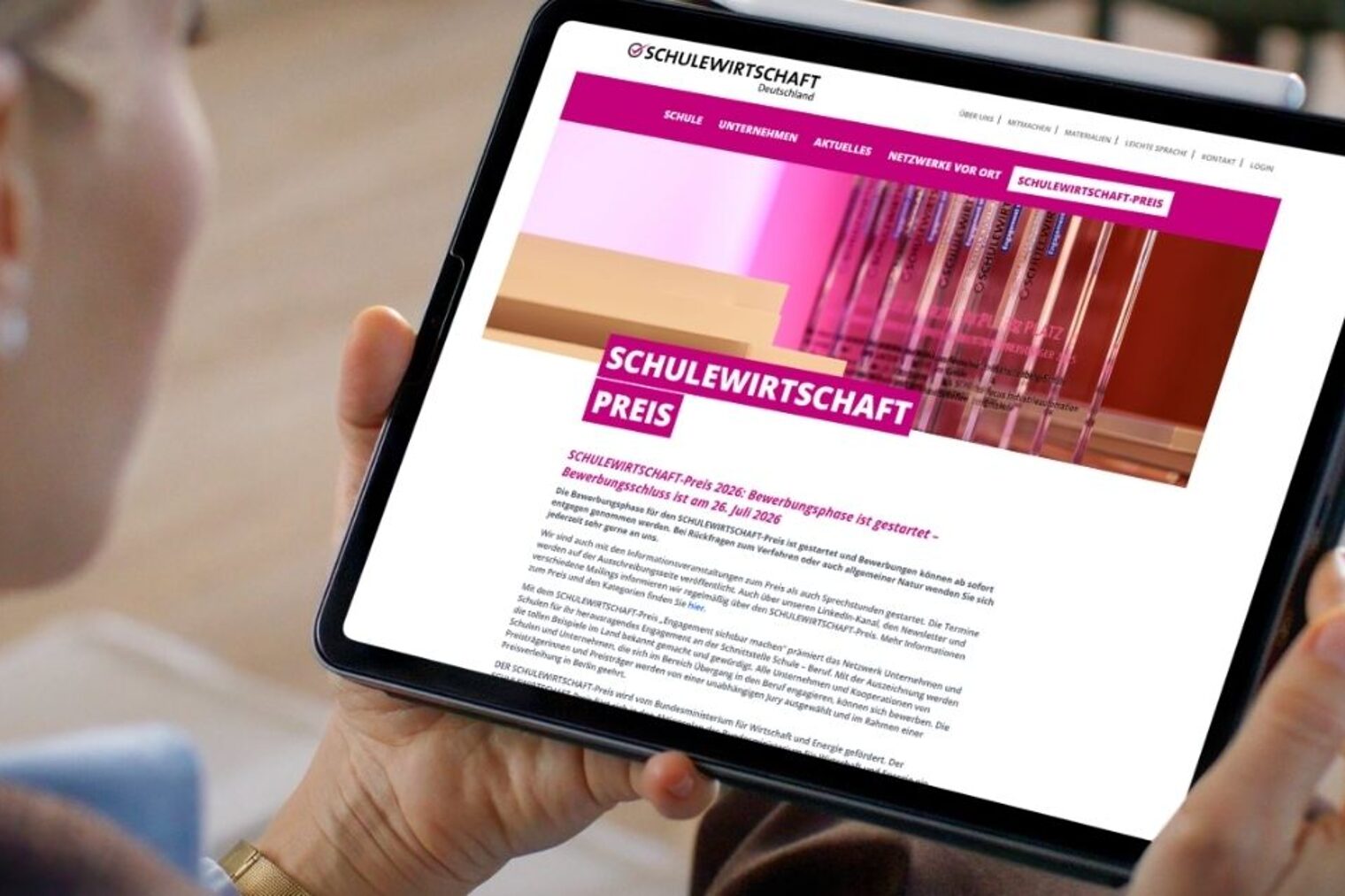 Frau schaut auf Tablet, auf dem die Startseite des Schulewirtschaft-Preises geöffnet ist