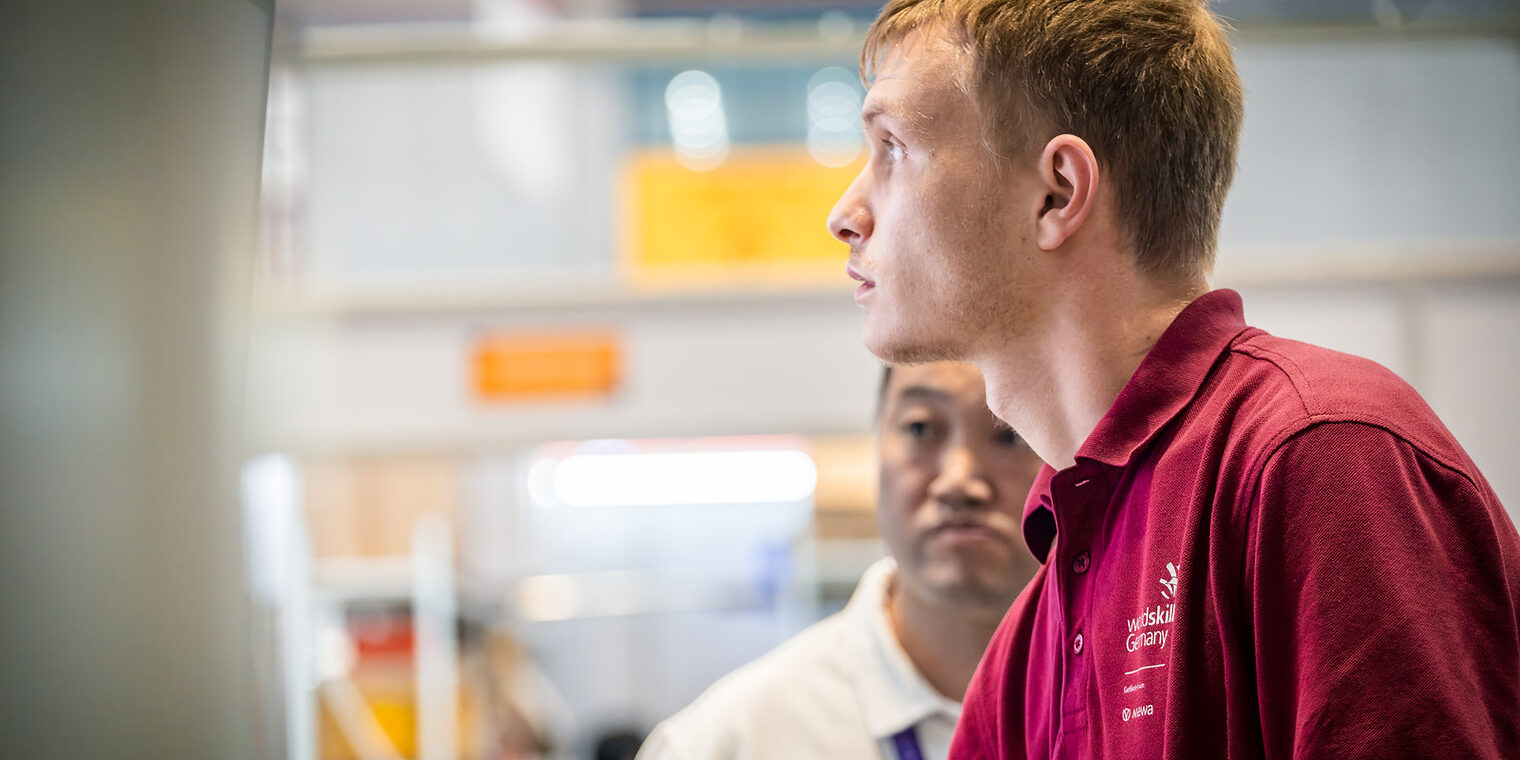 Junger Mann im Seitenprofil, Polohemd dunkelrot mit Aufschrift WorldSkills Germany, Lichtschein von vorne in sein Gesicht