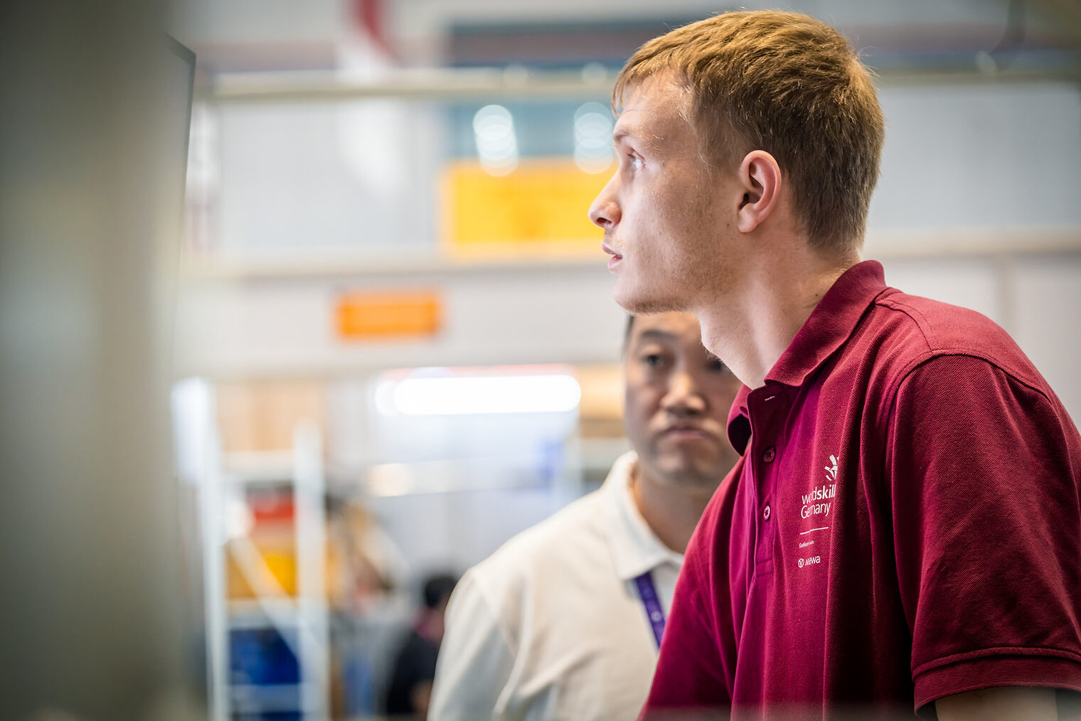 Junger Mann im Seitenprofil, Polohemd dunkelrot mit Aufschrift WorldSkills Germany, Lichtschein von vorne in sein Gesicht