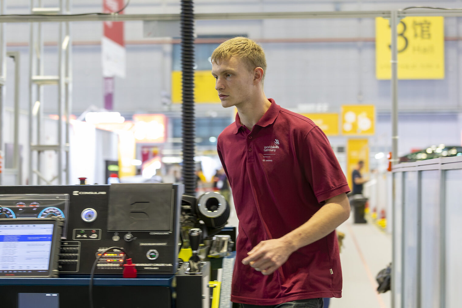 Junger Mann trägt rotes Polohemd, Aufschrift WorldSkills Germany in Bewegung, konzentrierter Blick